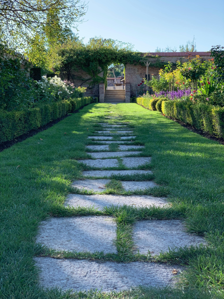 Peaceful garden with stone walkway, lush greenery, and vibrant flowers.