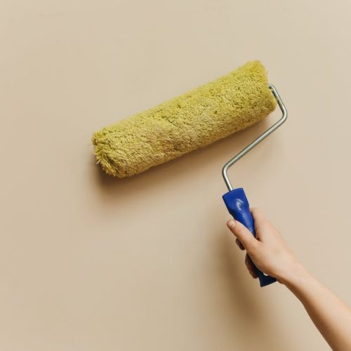 A hand using a yellow paint roller to paint a beige wall. Perfect for DIY and home improvement themes.